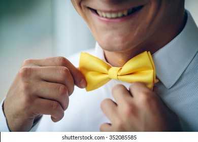 Portrait of happy smiling young man in a wedding costume and yellow butterfly tie over studio background. Closeup.Hands, lips, care, to correct, to adjust, fashion.