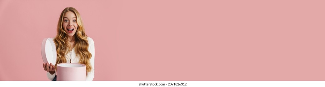 Portrait Of A Happy Smiling Young Woman Opening A Box Isolated Over Pink Background