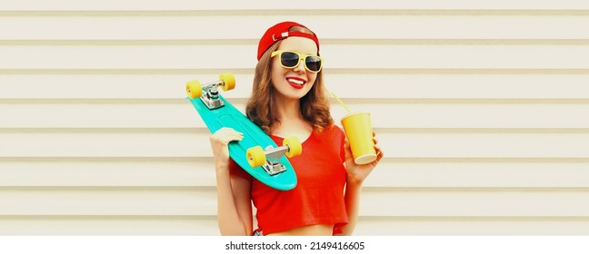 Portrait of happy smiling young woman with skateboard and cup of juice wearing red baseball cap, sunglasses on white background - Powered by Shutterstock