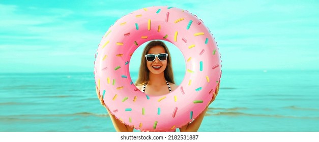 Portrait Of Happy Smiling Young Woman With Inflatable Ring Wearing Straw Hat On Beach On Sea Background