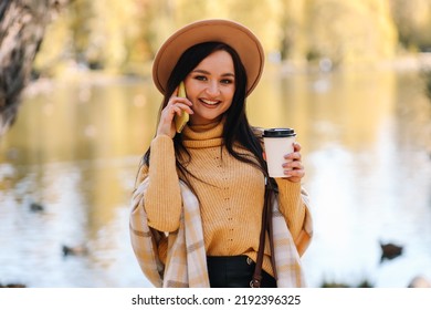 Portrait Of A Happy Smiling Young Woman Millennials In A Hat Laughing Talking Using A Mobile Phone Taking A Selfie Walking Alone In An Autumn Park In Nature In Autumn. Selective Focus