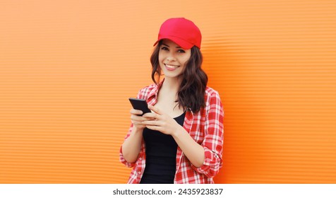 Portrait of happy smiling young woman with mobile phone in summer red baseball cap on colorful orange background - Powered by Shutterstock