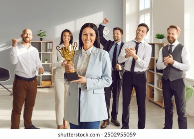 Portrait of a happy smiling young woman winner holding the trophy award for success in business standing in office with a team of people colleagues applauding for company best employee reward. - Powered by Shutterstock