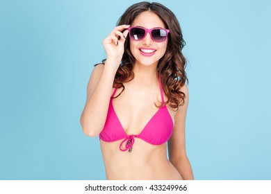 Portrait of a happy smiling young woman in sunglasses and bikini isolated on the blue background