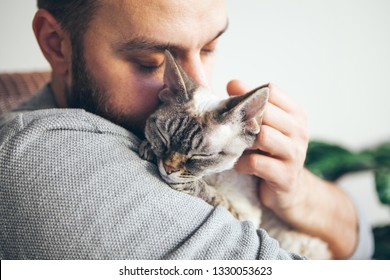 Portrait of happy snuggling cat with close eyes and young beard man. Handsome young guy is hugging and cuddling his cute color point Devon Rex Kitten. Domestic pets concept - Powered by Shutterstock