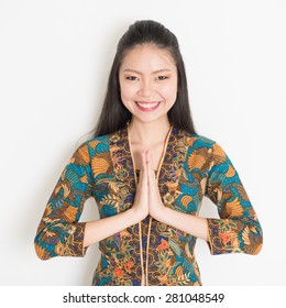 Portrait Of Happy Southeast Asian Woman With Batik Dress In Greeting Gesture On Plain Background.