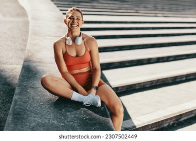 Portrait of a happy sports woman sitting outdoors. Athletic woman taking a break from jogging outdoors. Female runner working out in the morning. - Powered by Shutterstock