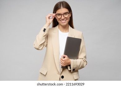 Portrait Of Happy Stylish Career Consultant Holding Closed Laptop In Hands On Gray Studio Background, Touching Glasses With Hand. Business And Technology