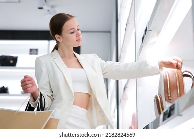 Portrait Of Happy Stylish Teen Fashionable Girl, Young Beautiful Pretty Woman In Mall, Enjoy Shopping With Bags Choosing Clothes, Backpack In Boutique. Shopaholic Lady Customer Buying In Shop, Store