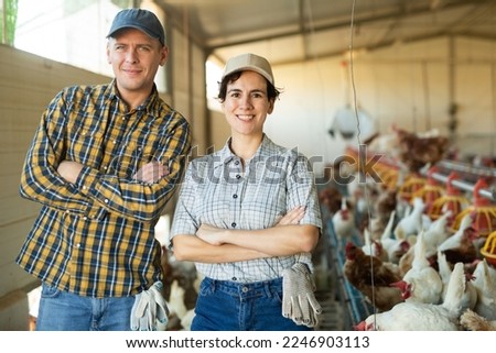 Portrait of happy successful biracial couple of farmers breeding laying hens in poultry farm, posing together in henhouse