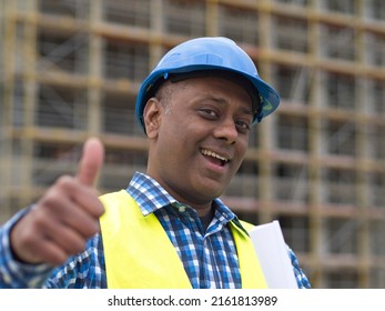 Portrait Of A Happy And Successful Indian Engineer Holding Rolled Up Plans, Smiling At The Camera And Showing A Thumbs Up Gesture