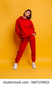 Portrait of happy tanned fit caucasian woman wearing trendy warm red fleece hoodie and pants, getting ready for cold winter. Studio bright shot, yellow background.