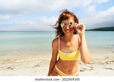 Portrait of happy tanned woman in sunglasses and yellow bikini smiling posing at sea beach - Powered by Shutterstock