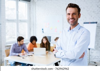 Portrait of happy teacher standing in classroom with students in background