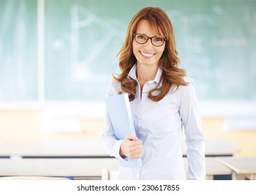 Portrait Of Happy Teacher Standing In Front Of Black Board While Holding Class Register. 