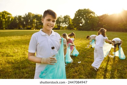 Portrait of happy teenage boy with gloves and trash bag looking cheerful at the camera holding plastic garbage in summer park with a children volunteers on background. Environmental pollution concept - Powered by Shutterstock