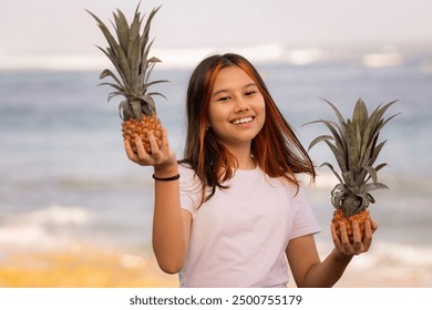 Portrait of happy teenager girl holding two whole pineapples. Smiling face. Blurred sandy beach, ocean and sky background. Organic fruit concept. Healthy lifestyle. Pandawa beach, Bali, Indonesia - Powered by Shutterstock