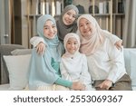 portrait of happy three different generations female muslim family meeting at home,sitting on couch in living room,hugging with love, smile,enjoy holiday time together