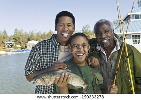 Portrait of happy three generation family with fishing rod and fish at lake