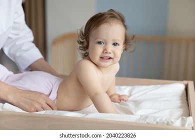 Portrait Of Happy Toddler Examined By Pediatrician On Baby Changing Table, Looking At Camera. Hands Of Nurse Undressing Child For Medical Checkup In Clinic Office. Infant Healthcare, Childcare Concept