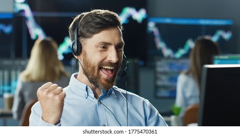 Portrait Of Happy Trader Or Broker Working At Stock Exchange Office Using Headset And Computer On Background Of His Business Team. Investment Entrepreneur Trading Concept.