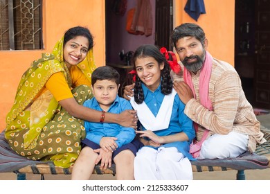 Portrait Of Happy Traditional Indian Parents Sitting With Their Young Daughter And Son In School Uniform, Mother Wearing Sari And Father In Kurta Teaching Kids,