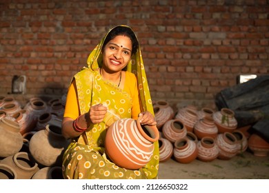 Portrait of happy traditional Indian woman potter artist painting and decorating design on clay pot for sale, handicraft, skill india. - Shutterstock ID 2126650322