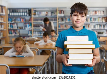 Portrait Of Happy Tween Boy Standing In Classroom With Books In Hands 

