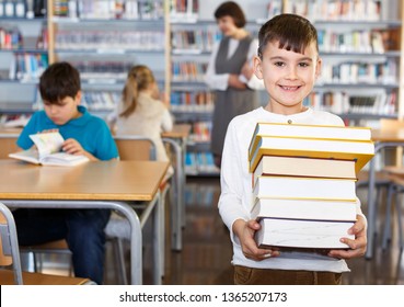 Portrait Of Happy Tween Boy Standing In Classroom With Books In Hands 

