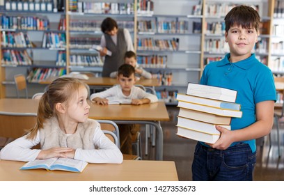 Portrait Of Happy Tween Boy Standing In Classroom With Books In Hands 

