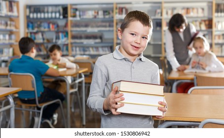 Portrait Of Happy Tween Boy Standing In Classroom With Books In Hands 

