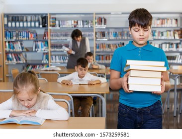 Portrait Of Happy Tween Boy Standing In Classroom With Books In Hands 

