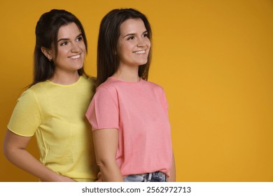 Portrait of happy twin sisters on orange background, space for text - Powered by Shutterstock