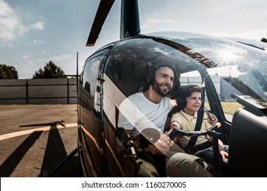 Portrait Of Happy Unshaven Father Embracing Glad Boy While Controlling Helicopter With Him. They Sitting In Cabin Of It While Talking. Optimistic Parent And Guy Wearing Earphones With Microphones