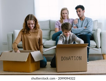 Portrait Of Happy Volunteer Caucasian Family Unpack, Packing Stuff Clothes In Cardboard Box Donate To Needy People While Sitting In Living Room At Home In Winter Day. Donation And Charity Concept.