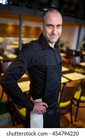 Portrait Of Happy Waiter Standing With Hands On Hip In Resturant