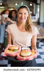 Portrait of happy waitress serving burgers in restaurant