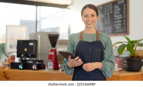 Portrait of happy waitress standing at restaurant entrance and holding digital tablet.  - Shutterstock ID 2251366989