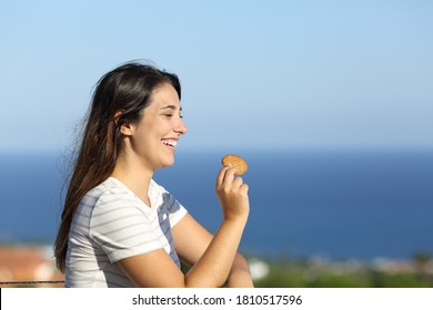 Portrait of a happy woman eats cookie in a hotel balcony on the beach