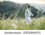 Portrait happy woman enjoying sunset stay on the green grass on the forest peak of mountain. Fresh air, Travel, Summer, Fall, Holidays, Journey, Trip, Lifestyle.