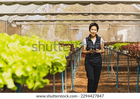 Portrait of happy woman farmer standing in organic vegetable farm and using smart phone