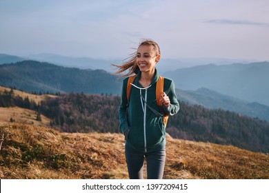 Portrait einer glücklichen Frau Wanderer, die auf dem Hang des Gebirges auf Bergen steht, blauer bewölkter Himmel auf dem Hintergrund. Die Frau ist glücklich und sieht sich die Kamera an. Reisen und aktives Lifestyle-Konzept.