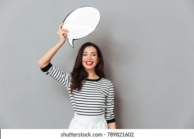 Portrait Of A Happy Woman Holding Blank Speech Bubble Above Her Head Isolated Over Gray Background