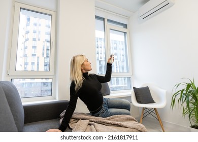 Portrait Of A Happy Woman Holding Remote Control In Front Of Air Conditioner At Home.