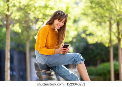 Portrait Of Happy Woman Looking At Mobile Phone In Park