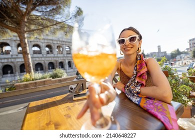 Portrait of a happy woman with Spritz Aperol at outdoor cafe near Coliseum, the most famous landmark in Rome. Concept of italian lifestyle and traveling Italy