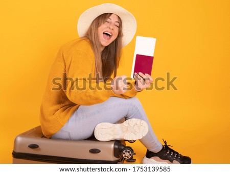 portrait happy woman, traveler with passport and suitcase, on yellow background