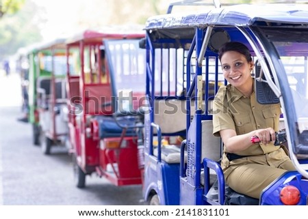 Portrait of happy woman in uniform driving six seater electric rickshaw
