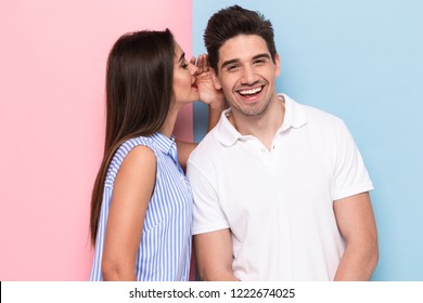 Portrait Of Happy Woman Whispering Secret Or Interesting Gossip To Handsome Man In His Ear Isolated Over Colorful Background