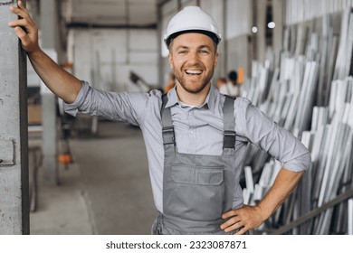 Portrait of a happy worker in a gray uniform and a white hard hat posing on the background of factory production - Powered by Shutterstock